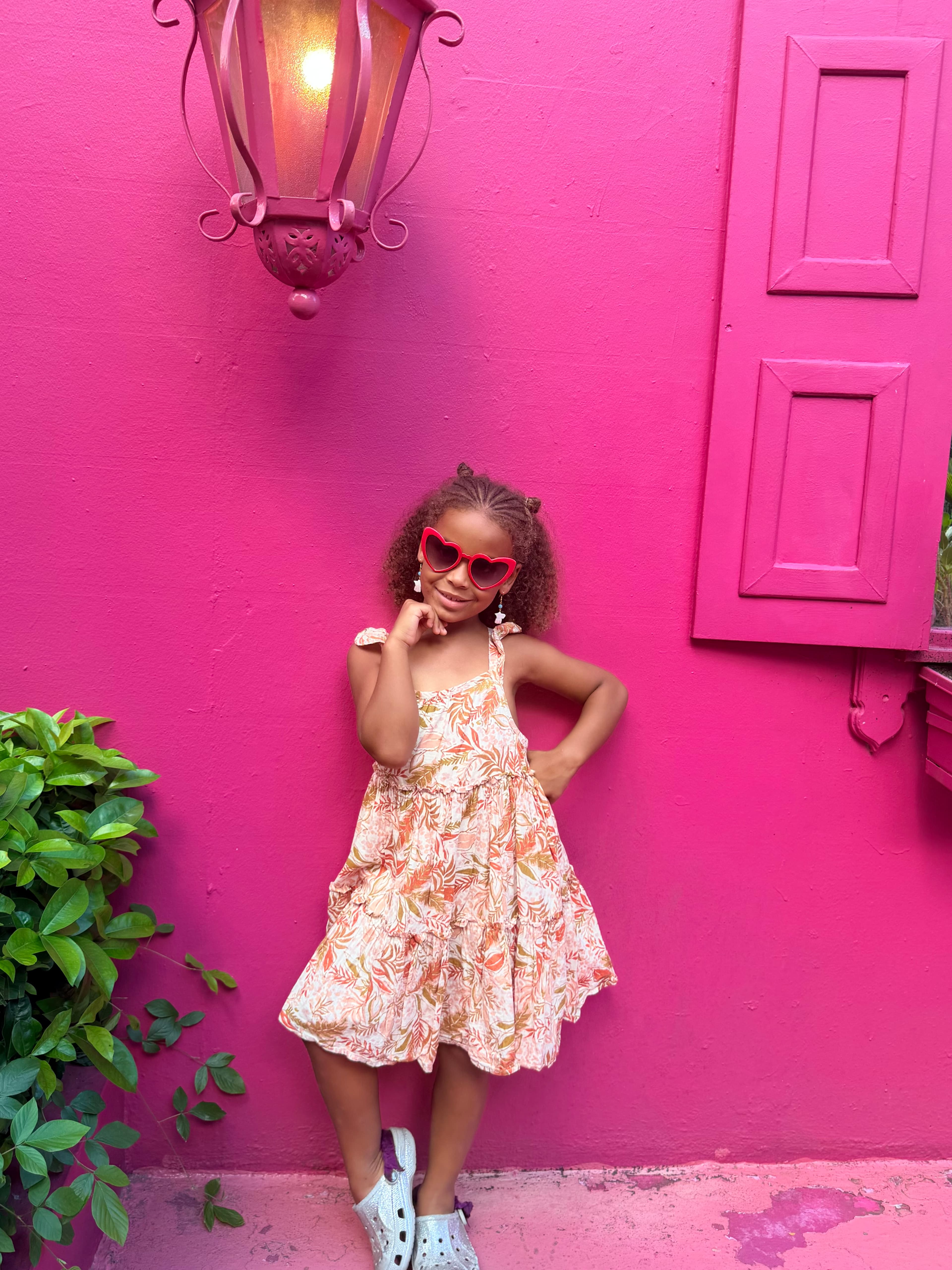 Kemi, age 7, in heart-shaped sunglasses against a pink wall